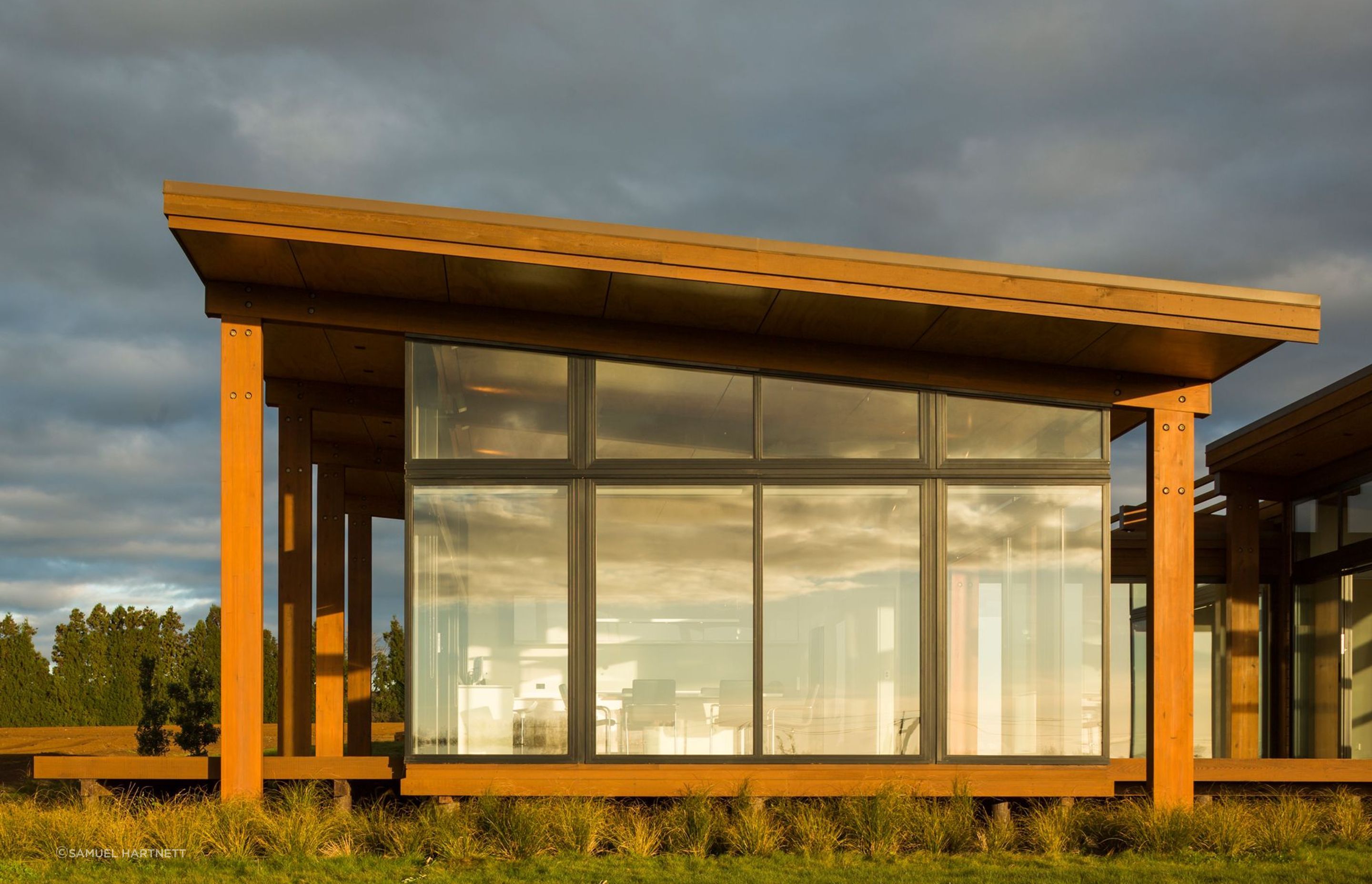 Macrocarpa posts frame the expansive full height glazing overlooking the surrounding landscape.