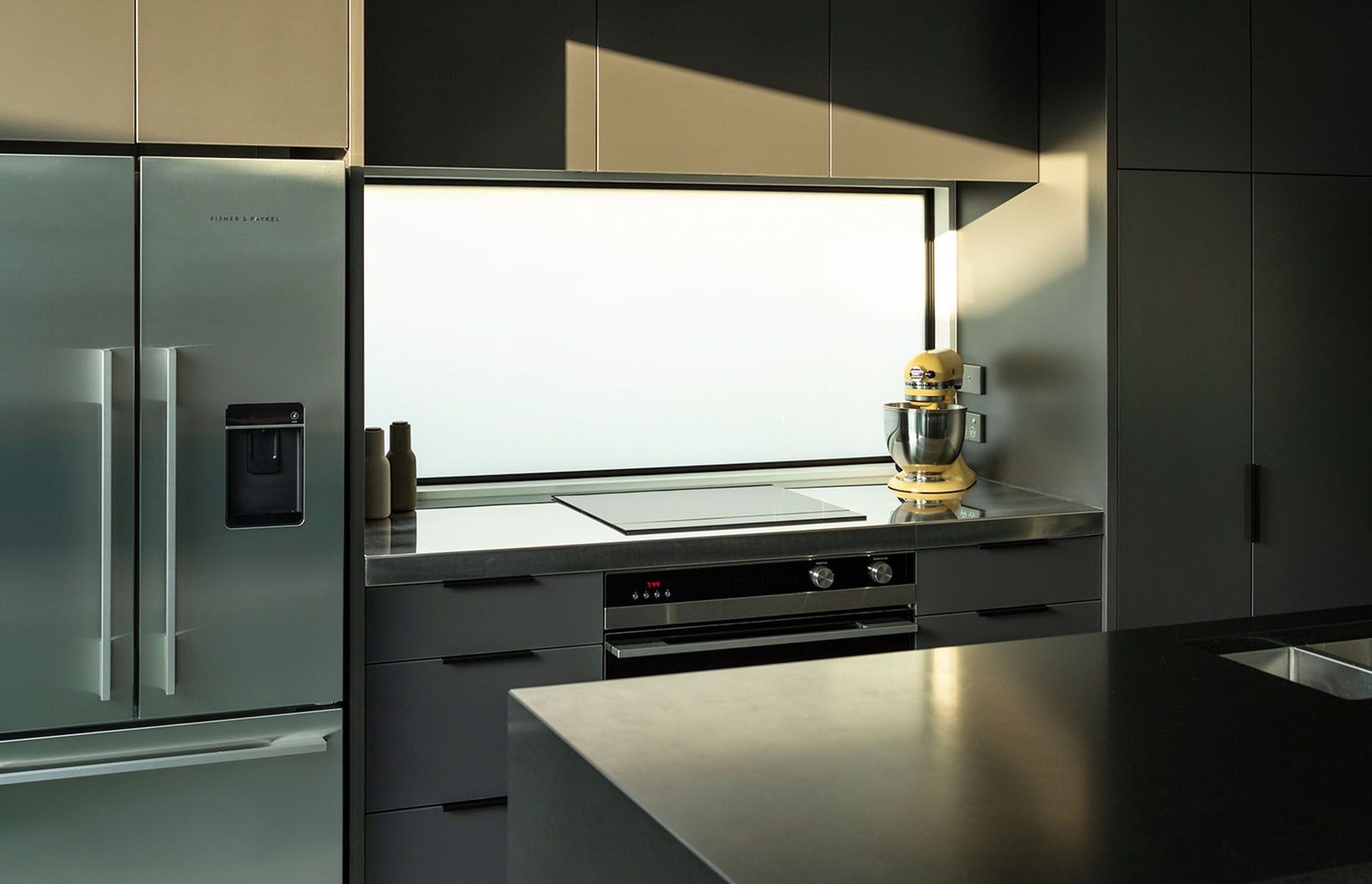 A reflective splashback and stone benchtop are complemented by Fisher &amp; Paykel appliances.