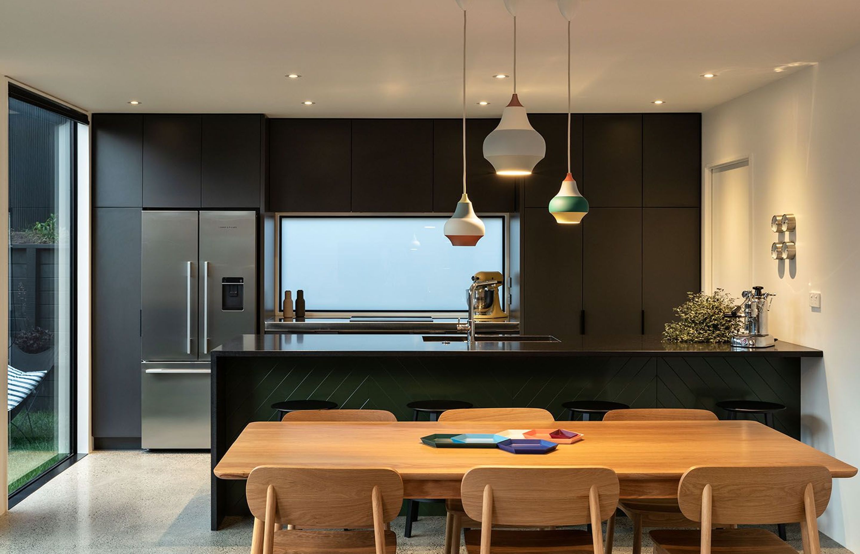 A dark green and grey kitchen draws on Blackbird's dark exterior, providing a contrast to the polished concrete flooring and timber table and chairs.