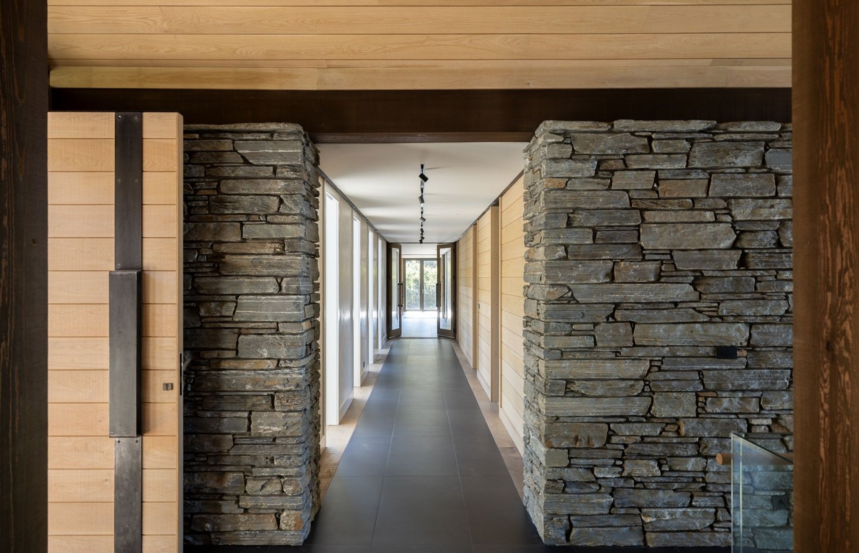 On both sides of the entry, a schist-clad wall anchors the home, with hallways leading to the bedrooms on the left, and living spaces on the right.
