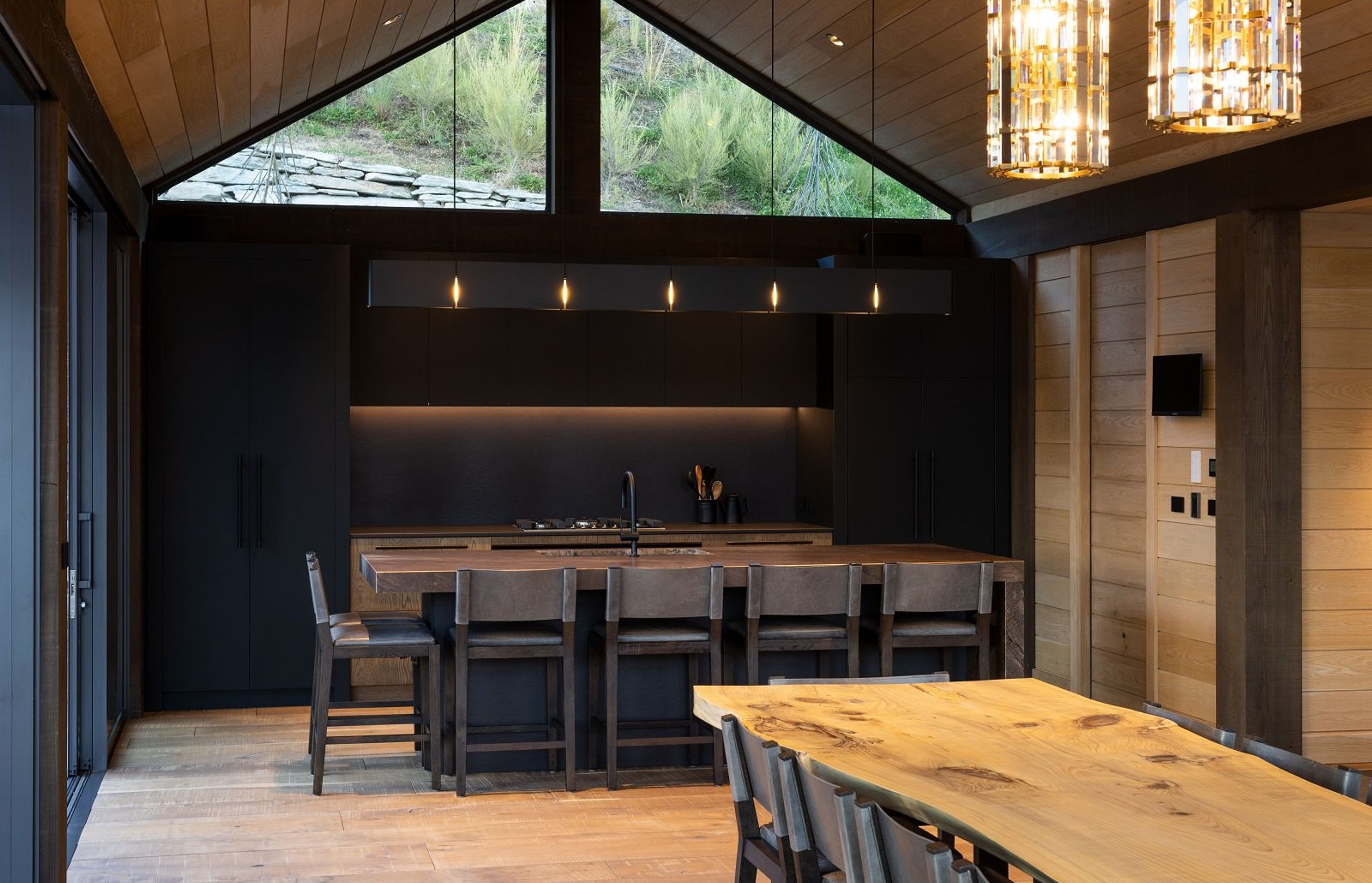 Adjacent to the main living space, the kitchen, with its dark and moody colour palette, is recessed back towards the hill.