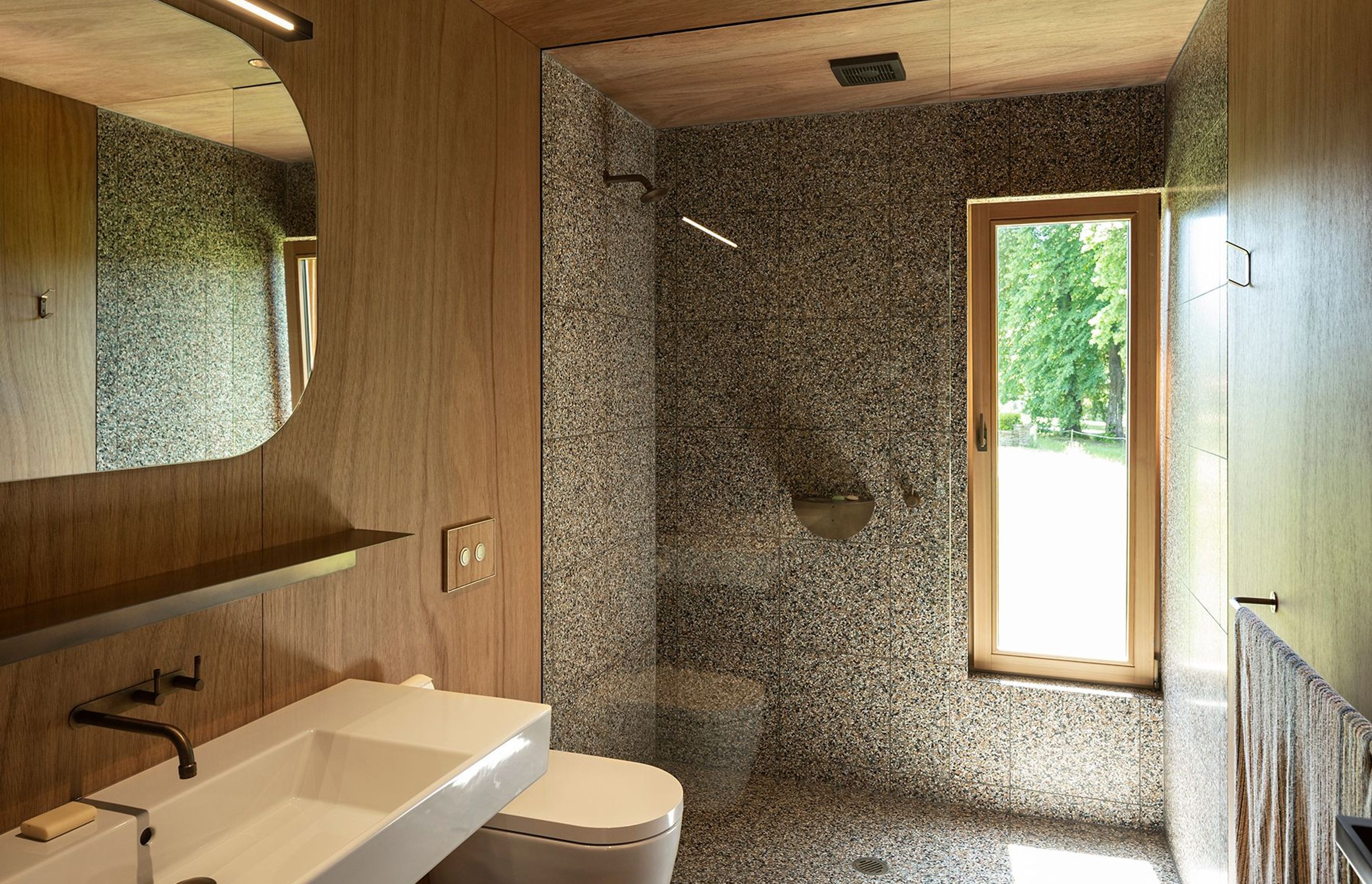 Timber cabinetry continues into the bathroom space with its distinctive speckled tiling and bronze tapware.