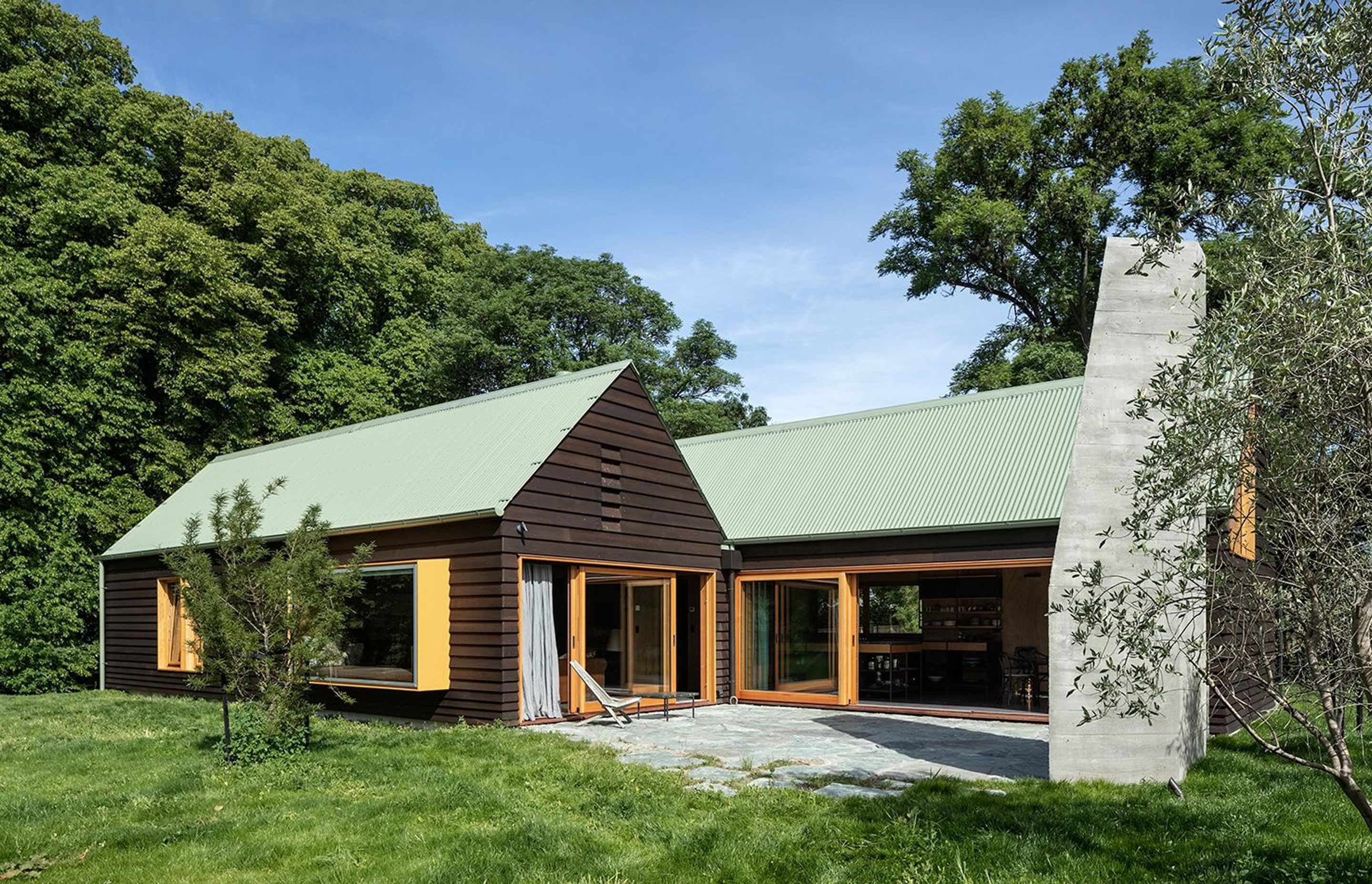 Chocolate-brown cedar weatherboards, sage-green metal roofing and mustard-yellow windows add familiarity to this cosy family dwelling in Wanaka.