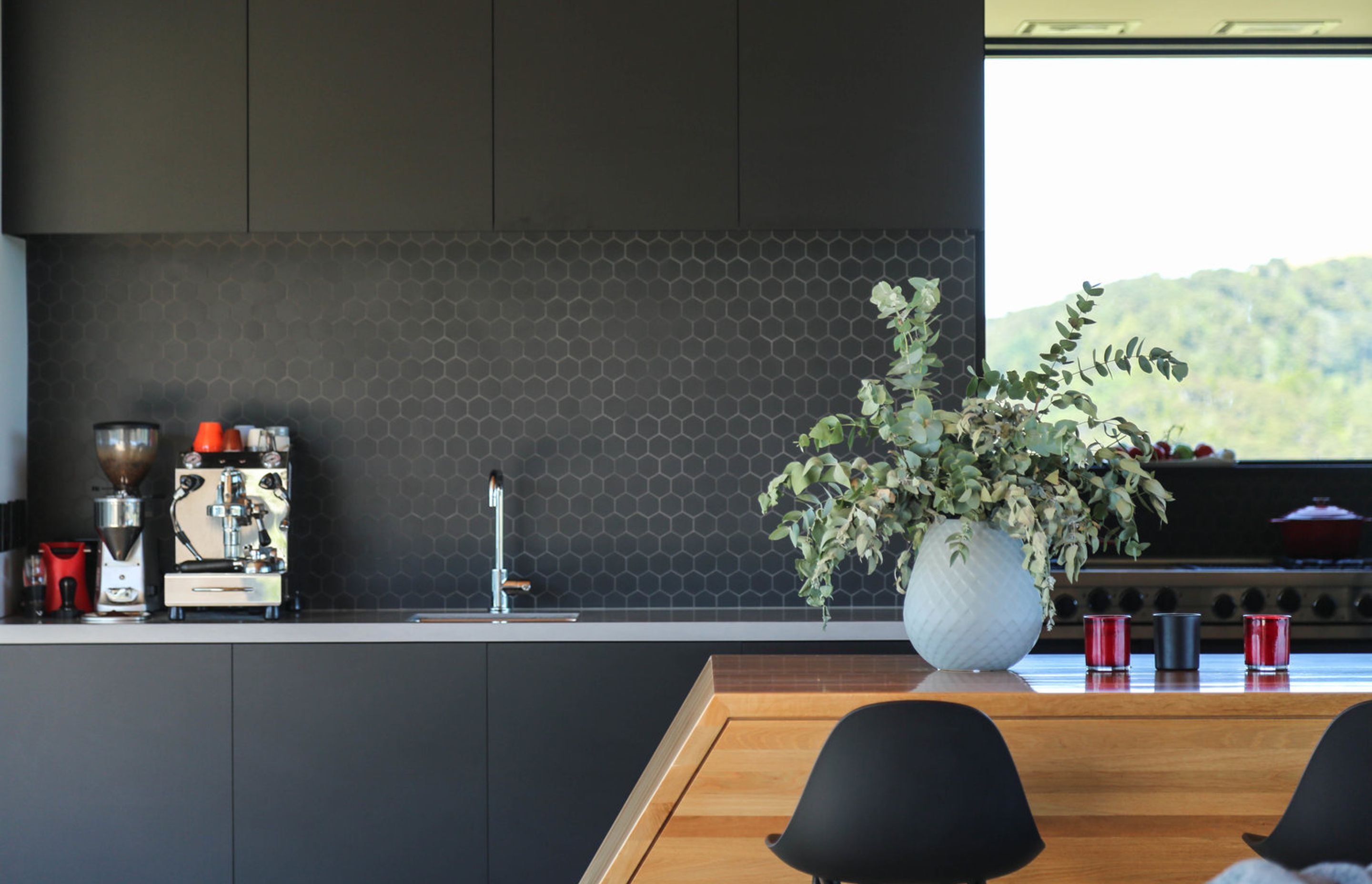 The kitchen features bespoke black cabinetry, black hexagonal tiling, and a sloping bar made from Southland beech.