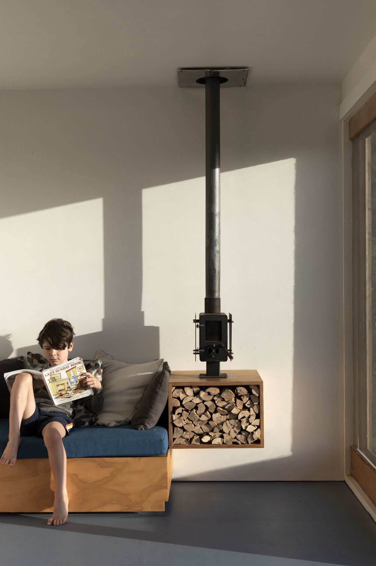 The owners's son enjoying some reading on the bespoke sofa, which features an adjacent fireplace and wood storage.