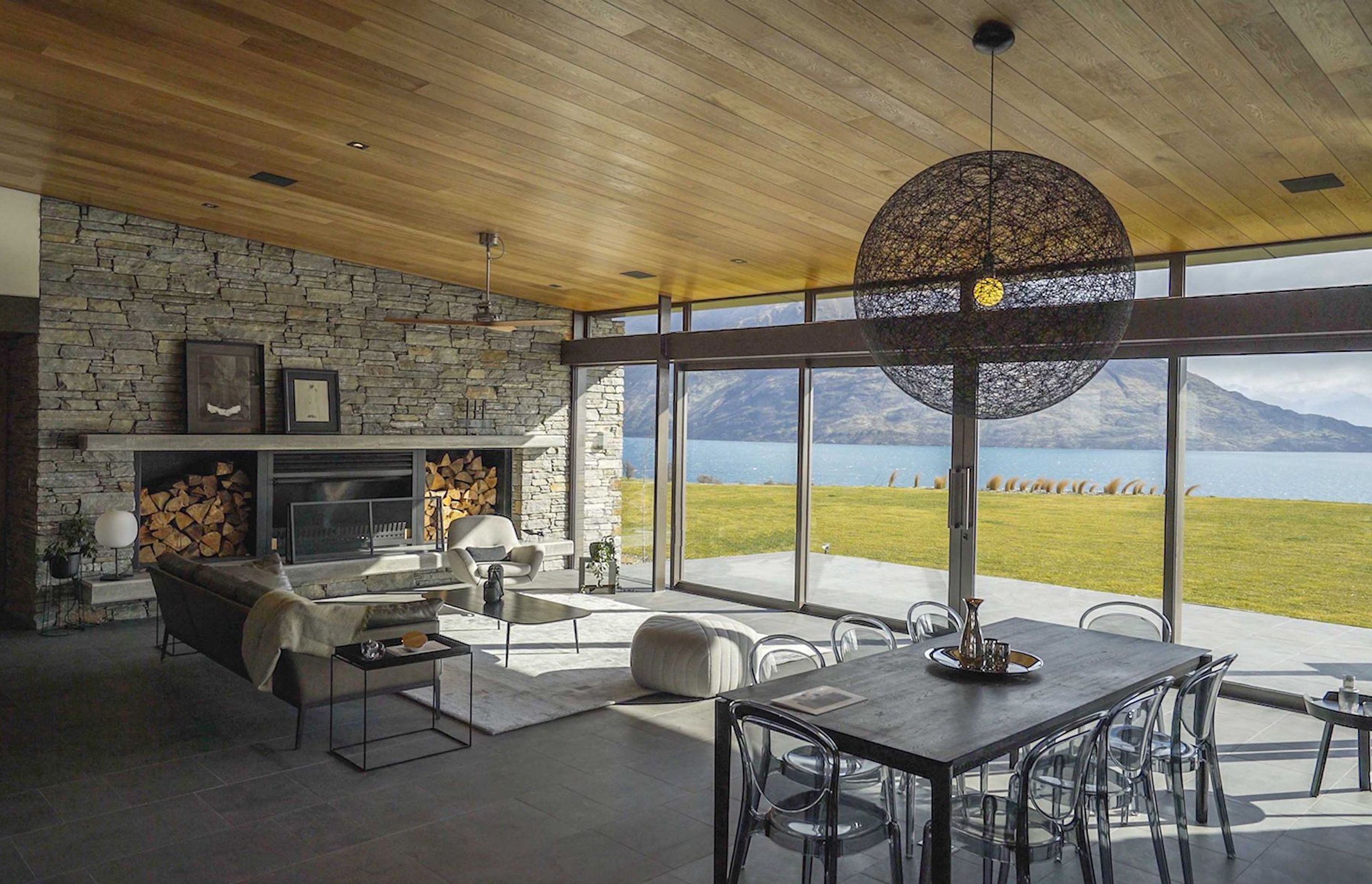 The dining and living area looks out to Lake Wakatipu. A natural palette of schist, timber and stone helps to blend the interior in with the surrounding landscape. AP.