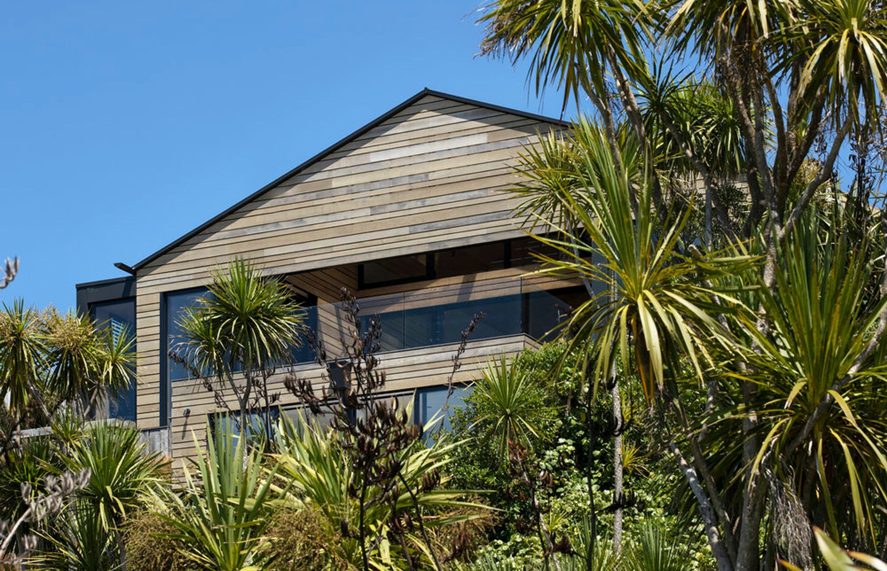 Horizontal cedar and glass define this elevation, complementing the greenery and light palette of the coastal area.