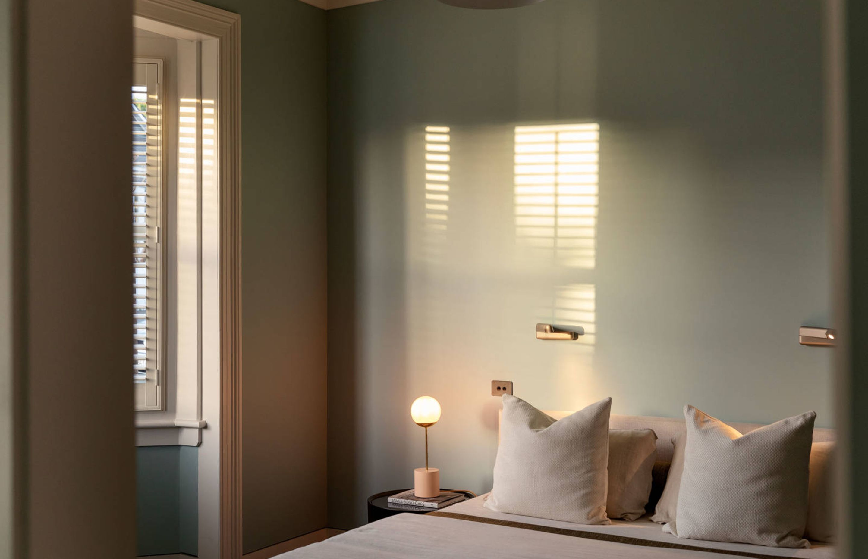 A master bedroom in the original villa features soft green walls that tie in with the exterior paint colour.
