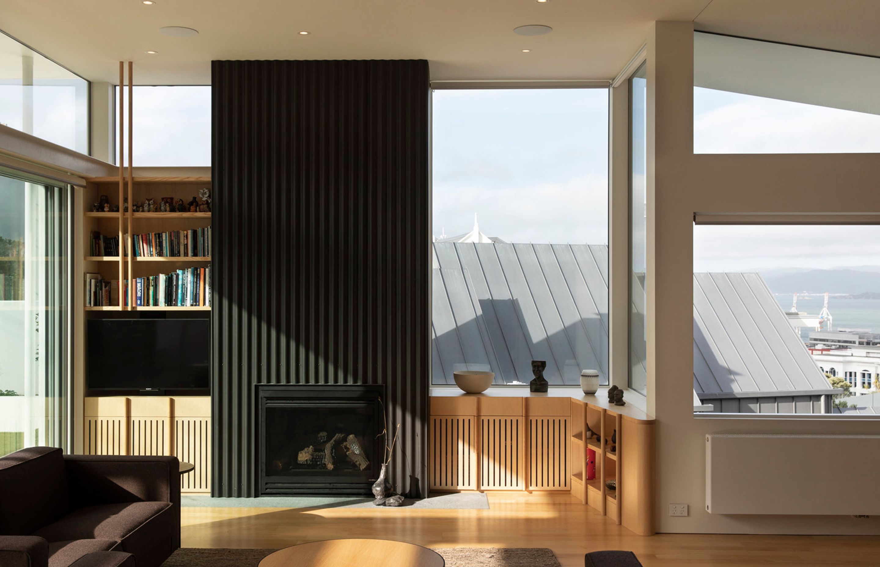 In the living room of the upstairs apartment, the vertical lines of the zinc corrugate clad fireplace and American ash bookcase continues the verticality of the exterior cladding.