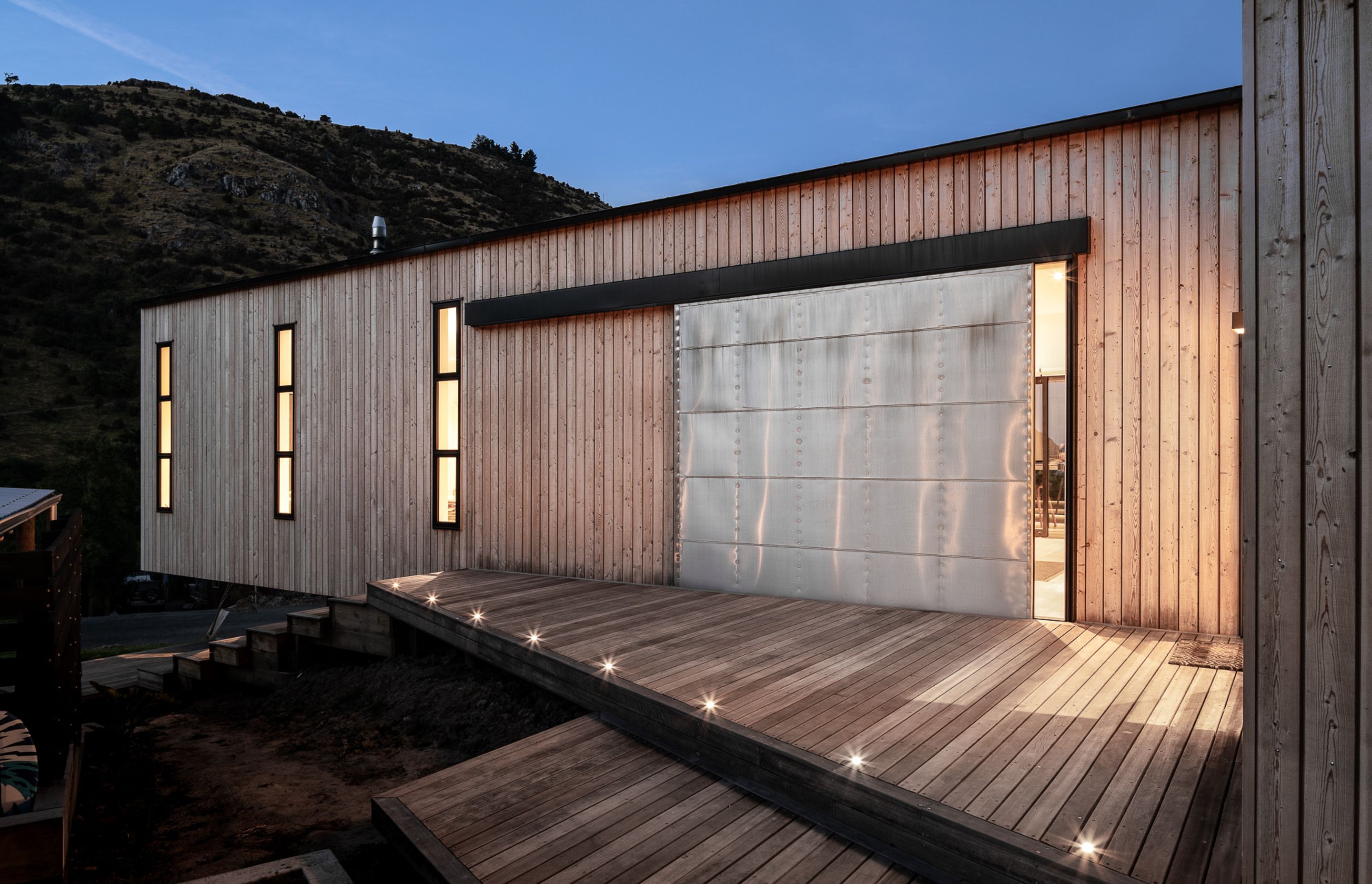 The western elevation, facing the valley, features a large industrial door that was designed by the architect and custom-built with pure zinc cladding and expressed rivets and seams.