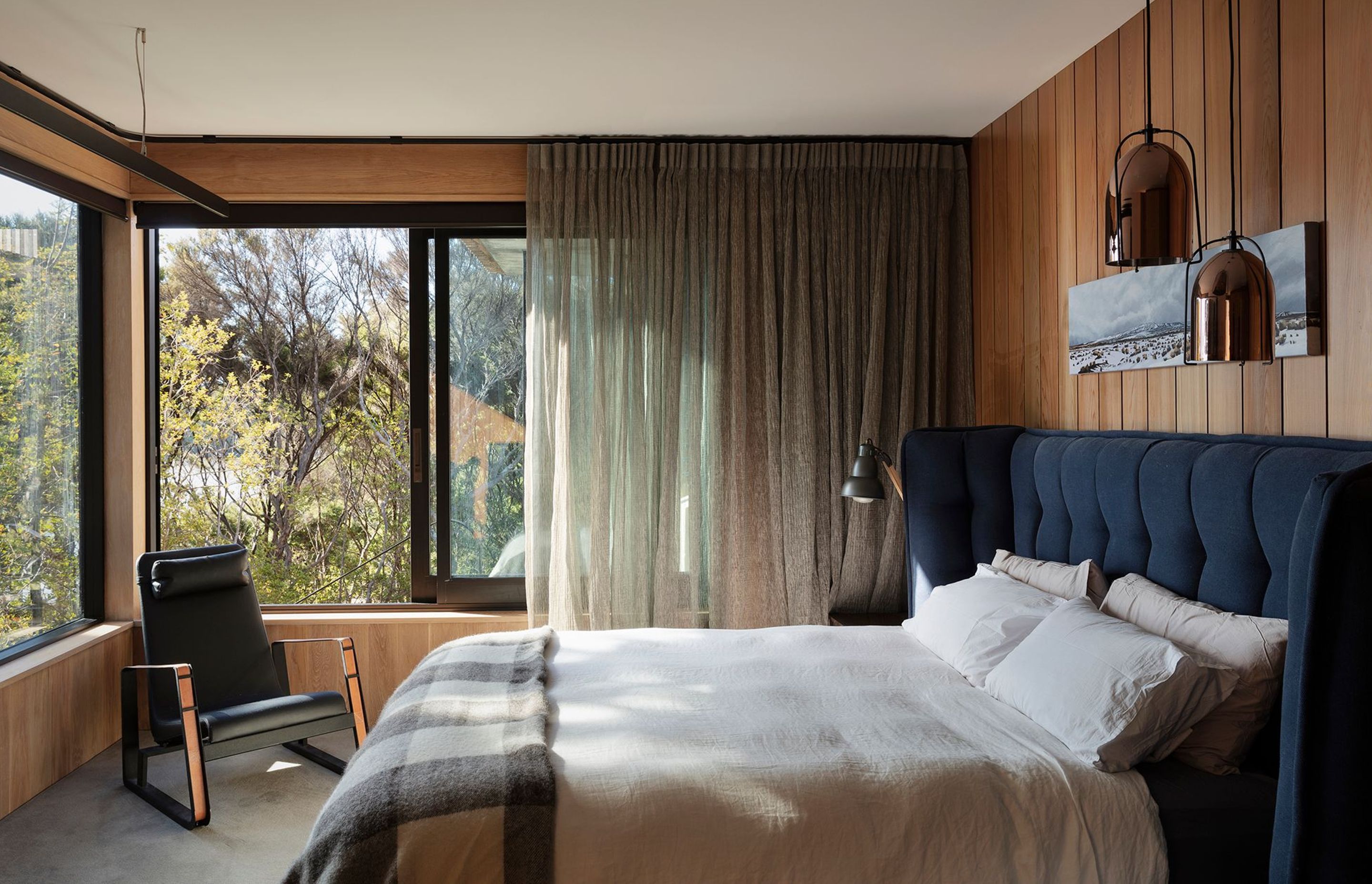The bedroom is lined with timber panelling and enjoys views over the bush through large windows.