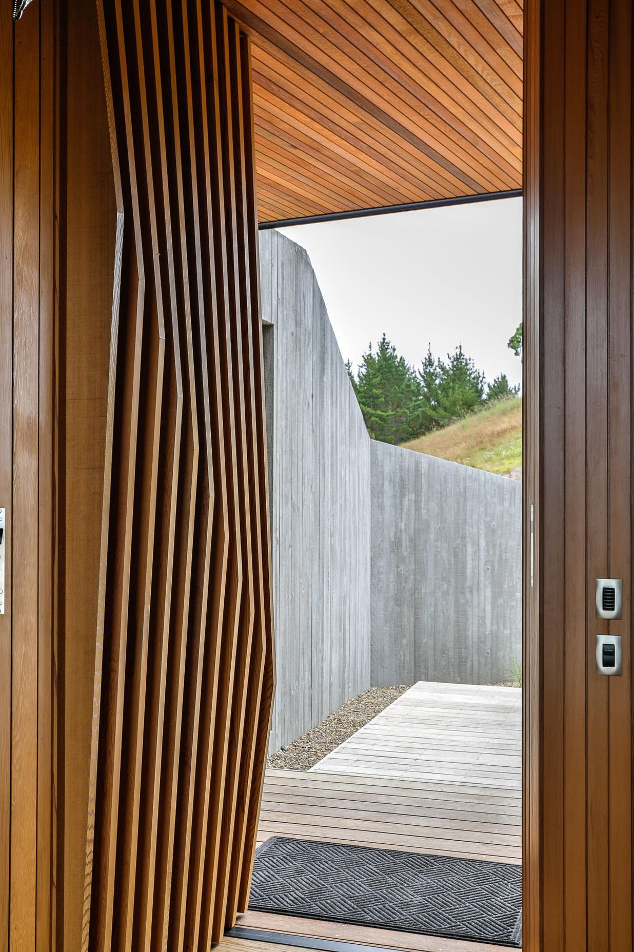 The faceted cedar fins on the main entry door each have a slighty different angle, playing on the vertical in situ formwork pattern of the spine entry wall.