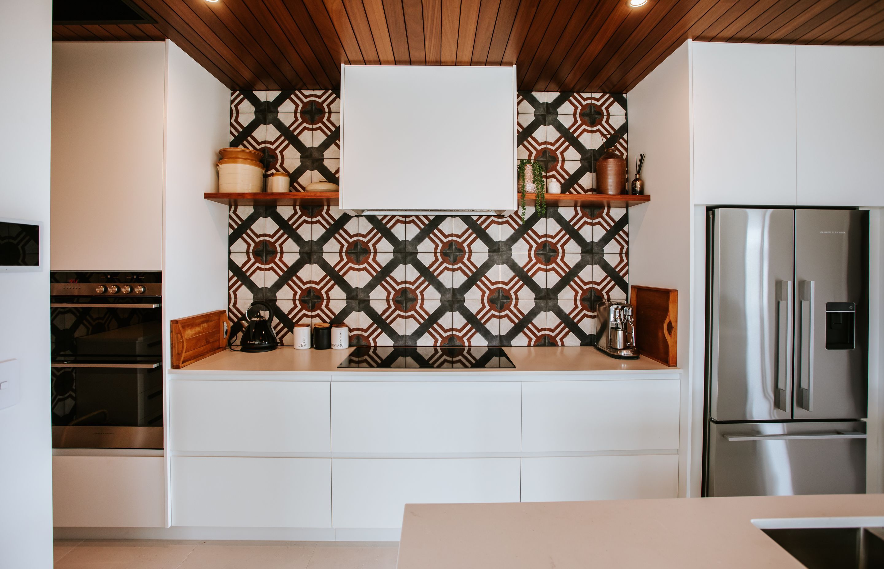 The kitchen features a timber ceiling that delineates the space and combined with the highly patterned tile splashback, the materials create a warm and textured feel.
