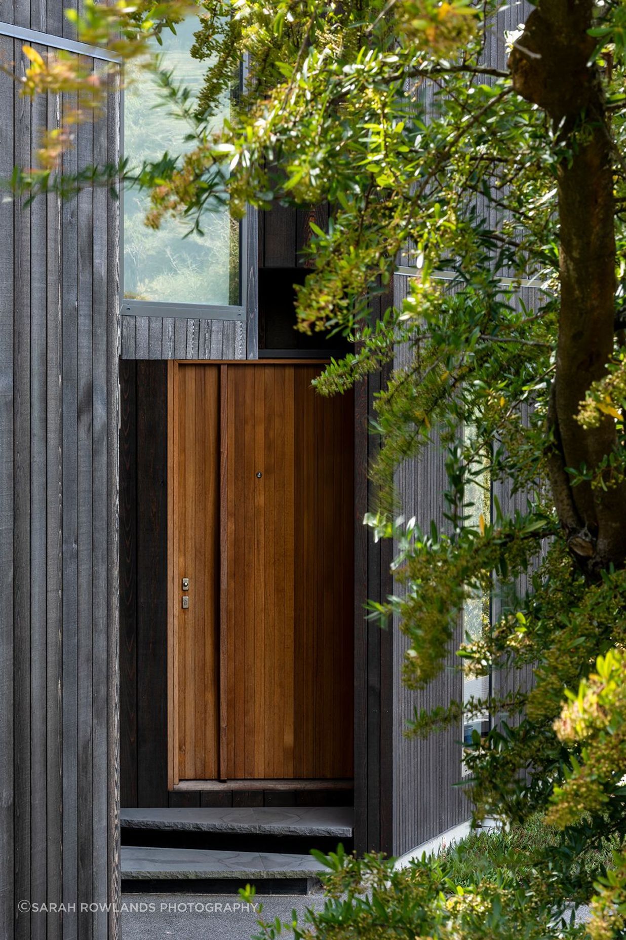 The discreet entryway is folded into the house, with a contrasting stain front door to mark the entrance.