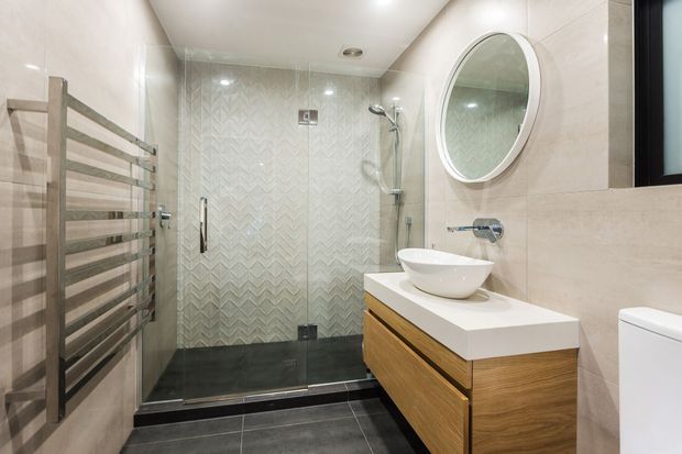 Contemporary bathroom featuring a glass-enclosed walk-in shower with patterned wall tiles, dark floor tiles, a heated towel rail, a floating timber vanity with a white vessel basin, and a round wall mirror.