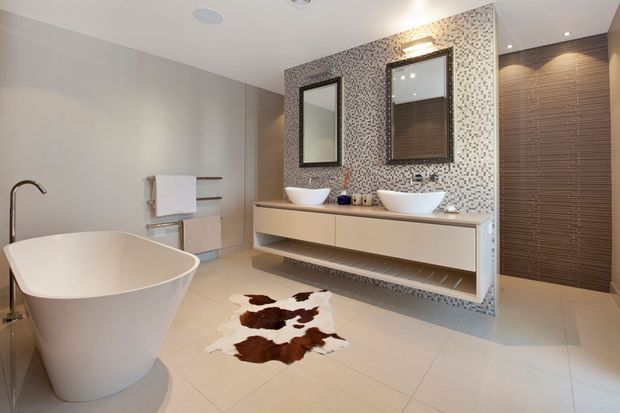 Contemporary luxury bathroom featuring a freestanding white bathtub, double vessel basins on a floating vanity, large mirrors, a patterned mosaic feature wall, neutral large-format floor tiles, and a dark timber-toned louvred privacy screen or door.