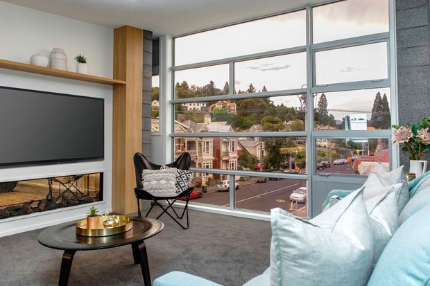 Contemporary living room with a large sectional sofa, black coffee table, fireplace and television built into a timber feature wall. Floor-to-ceiling steel-framed glazing overlooks an urban neighbourhood, while a butterfly chair and decorative shelving complete the space.