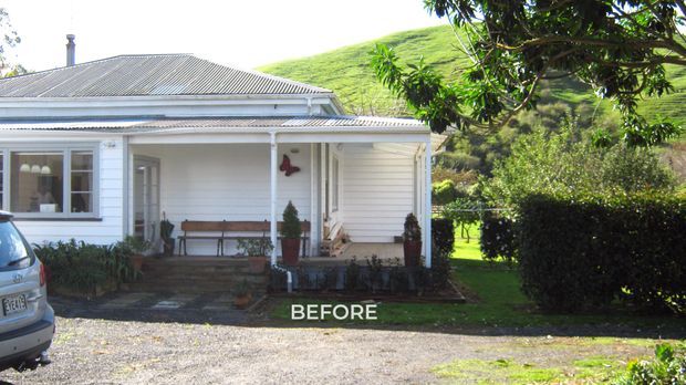 A front exterior view of a modest single-storey white weatherboard house with a corrugated metal hipped roof, covered entry porch, timber-framed windows, and a small front garden. A vehicle is partially visible at the left edge, while a green hillside rises behind the property. The image is labelled “BEFORE,” suggesting a renovation or alteration project.