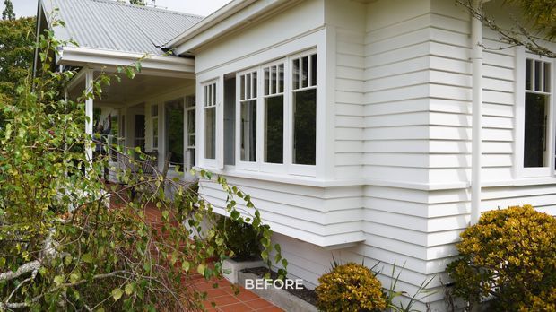Exterior view of a traditional single-storey home clad in white horizontal weatherboards, with a light grey corrugated metal roof, white-framed multi-pane windows, a covered entry porch, and a red brick path surrounded by established planting. The image is labelled “BEFORE.”