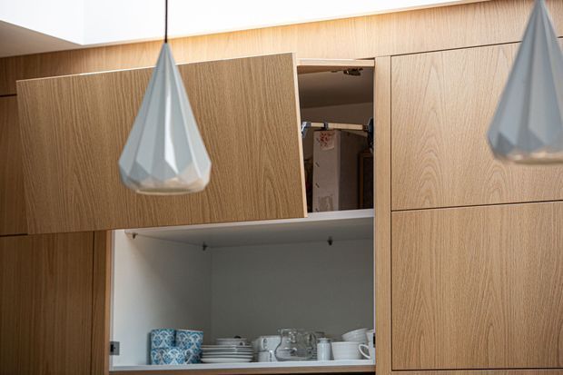 Close-up of built-in light timber cabinetry with open shelving displaying crockery and glassware. Two faceted pendant lights hang in front of the joinery, creating a refined contemporary kitchen or dining storage feature.