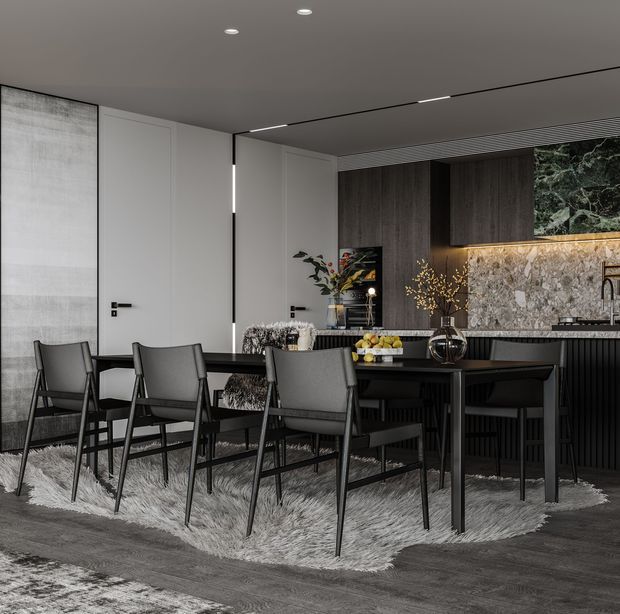 A sophisticated open-plan dining and kitchen interior with a dark, monochromatic palette. A black dining table is surrounded by upholstered dining chairs over a textured light rug. Behind it, the kitchen features dark wood cabinetry, black ribbed joinery, a stone benchtop and splashback, integrated appliances, and warm under-cabinet lighting. White paneled doors and a large abstract wall artwork contrast with the darker finishes.