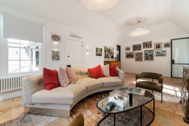 Bright, carefully styled living room with a large cream sectional sofa, colourful cushions, patterned area rugs, a glass-topped coffee table, framed artwork, and a gallery wall. White-painted walls, ceiling panelling, traditional window proportions, and a radiator create a refined classic interior, while contemporary furniture and lighting keep the space fresh and inviting.