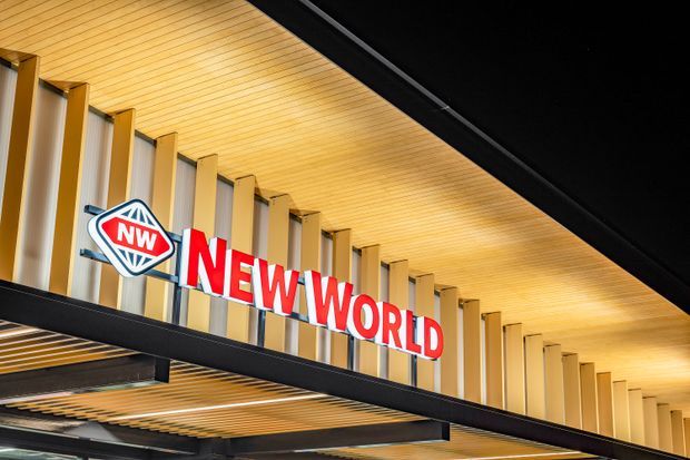 Exterior view of a New World supermarket entrance canopy, featuring prominent red-and-white New World signage, a warm timber-look slatted soffit, vertical facade fins, and dark structural steel framing.