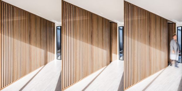 Triptych-style image of a bright contemporary interior corridor featuring a full-height vertical timber batten screen or partition, pale flooring, white ceiling, and narrow black-framed glazing at the end. A blurred person is visible in the right panel.