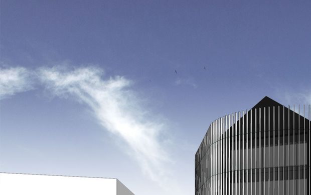 Exterior architectural view dominated by a modern curved building facade with closely spaced vertical metal fins and a dark pitched or angular roof form. A simple white neighboring structure is partially visible at left beneath a clear blue sky.