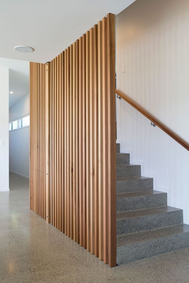 Bright contemporary stairway and hallway featuring a sculptural vertical timber batten screen, polished grey terrazzo or concrete stairs and flooring, white walls, and a simple timber handrail. The open slatted partition creates a strong architectural feature while allowing views toward the adjacent corridor.