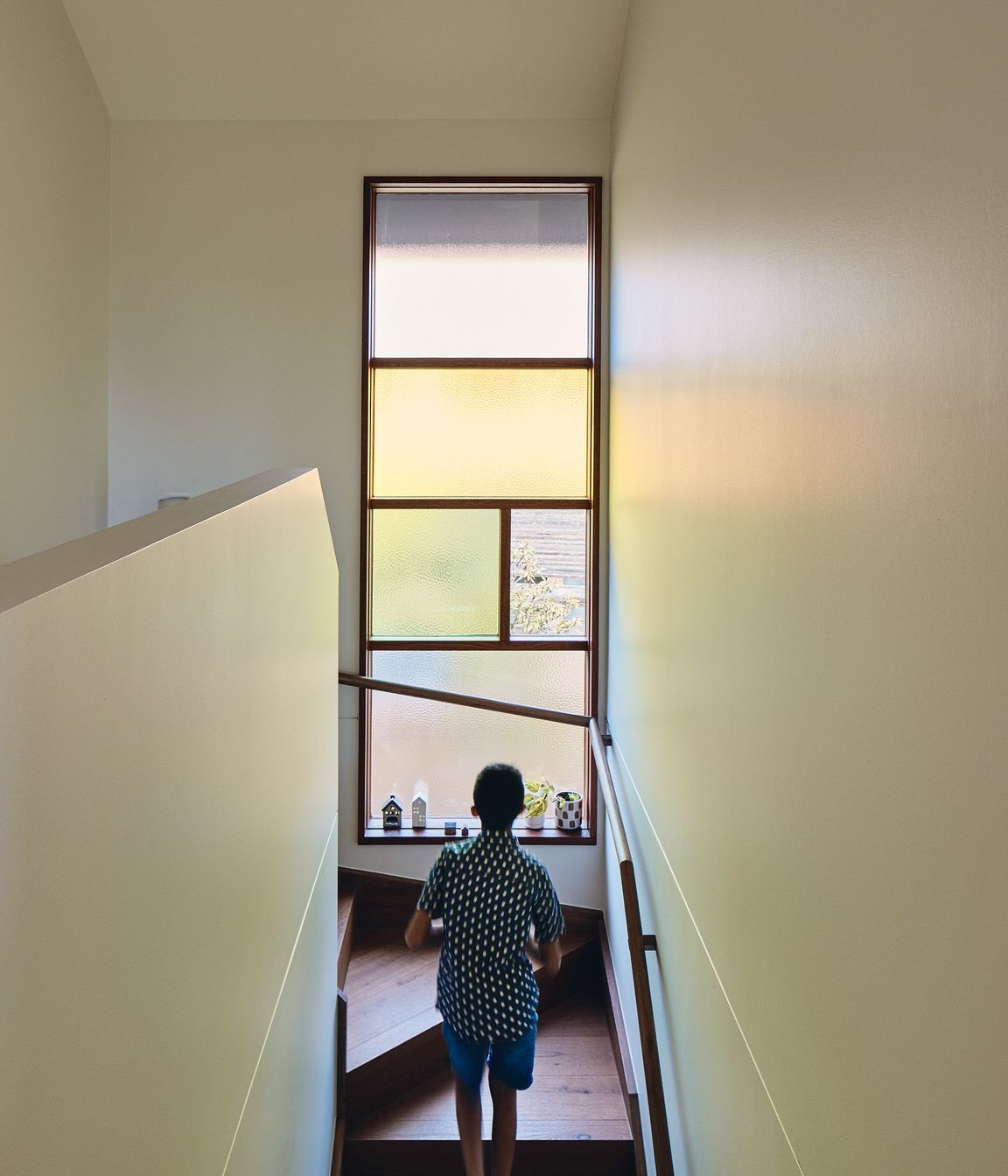 Coloured glass within the stairway and kitchen windows, along with a skylight shaft bathing the home’s entry in warm light, introduces zesty oranges, greens, reds and yellows into daily life.