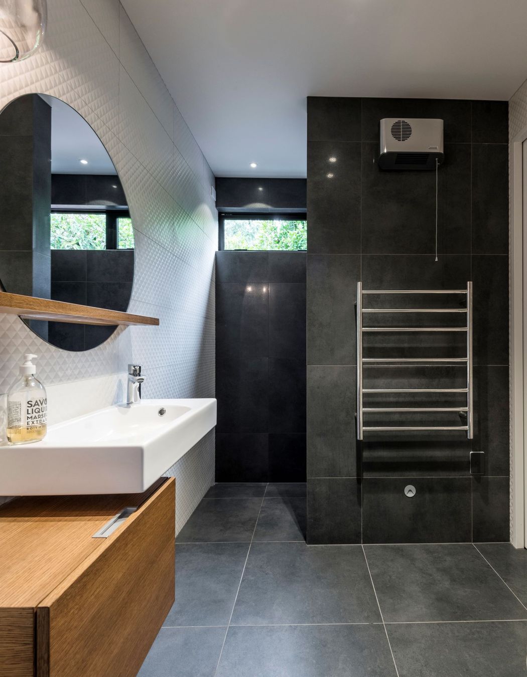 This bathroom features a porcelein vanity that is offset from the timber cabinetry; and floor to ceiling tiles.