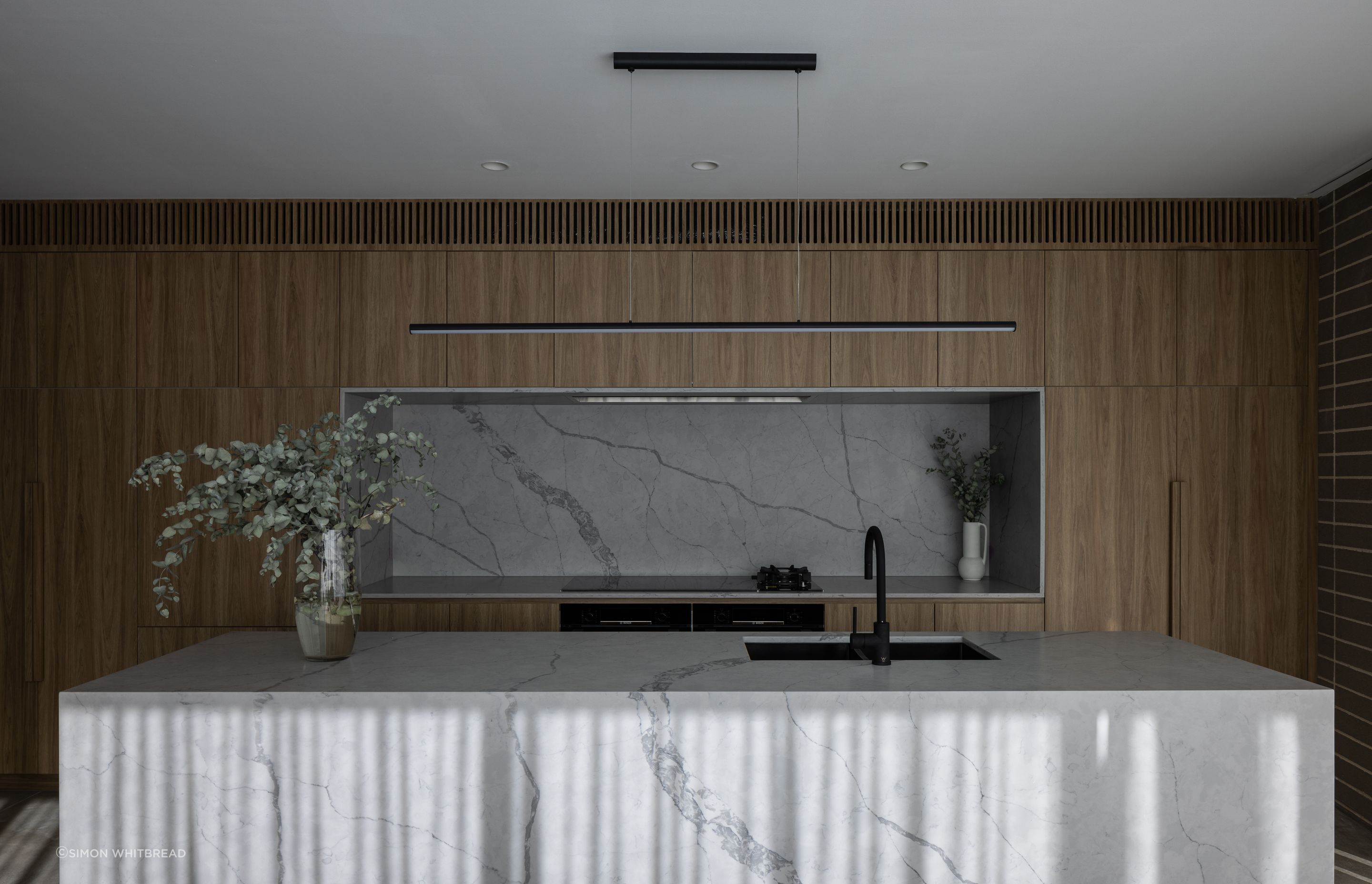 Solid materiality softened with warm timber tones.