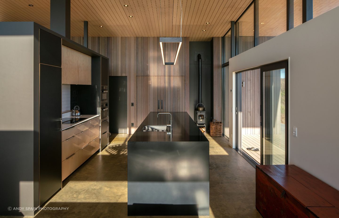 The kitchen in Te Horo Beach House by First Light Studio has an over-benchtop LED light feature and ceiling spotlights to create a dramatic atmosphere.