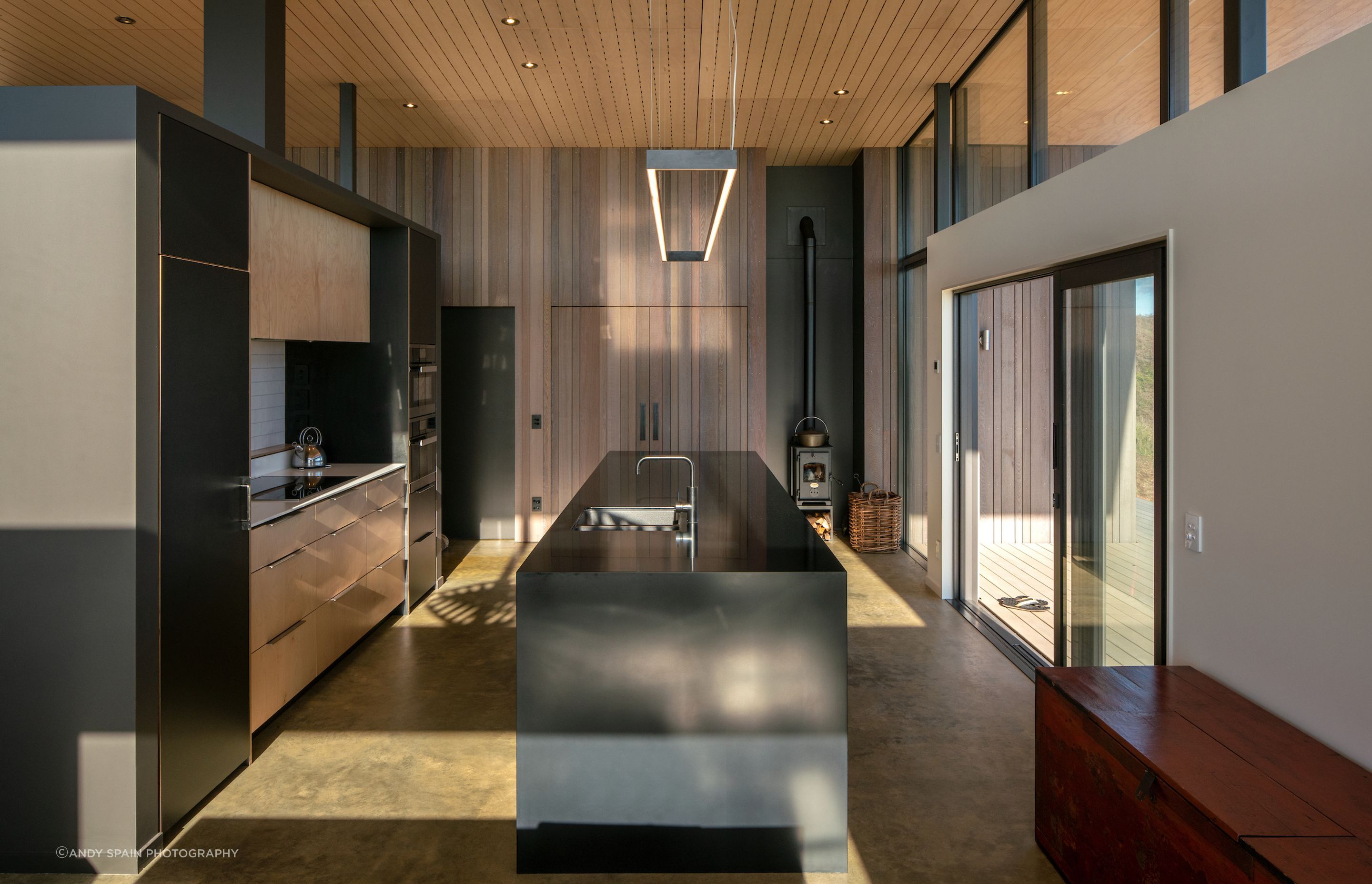 The kitchen in Te Horo Beach House by First Light Studio has an over-benchtop LED light feature and ceiling spotlights to create a dramatic atmosphere.