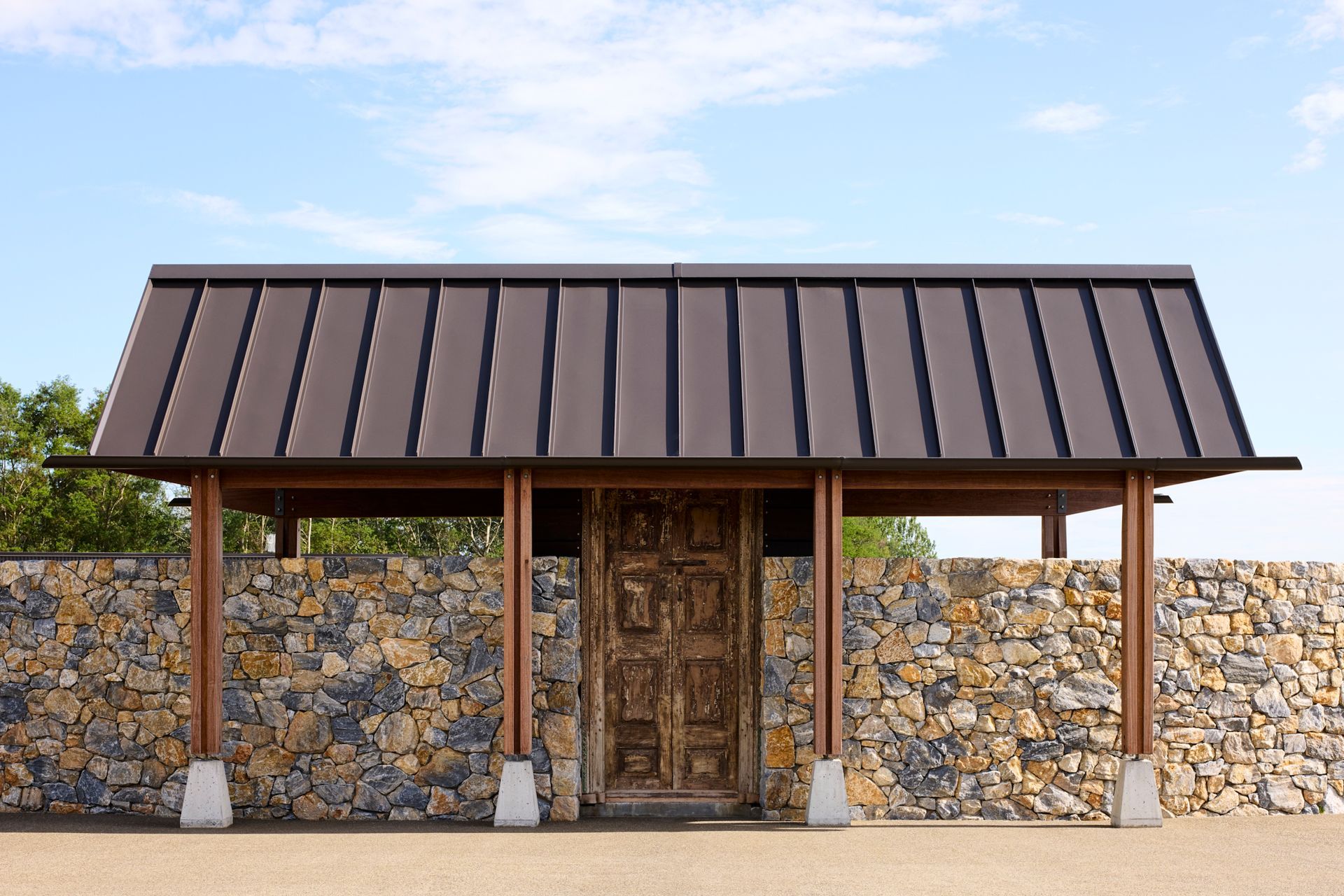The beautiful, architecturally designed woodshed features a curved stone wall, with timber posts sitting on elegantly formed concrete plinths, holding up the roof.