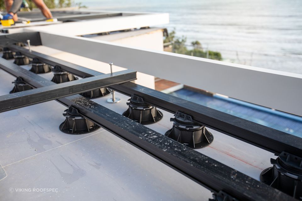 The aluminium frame system supports floating deck surfaces using timber or composite planking, structural tiles or pavers.