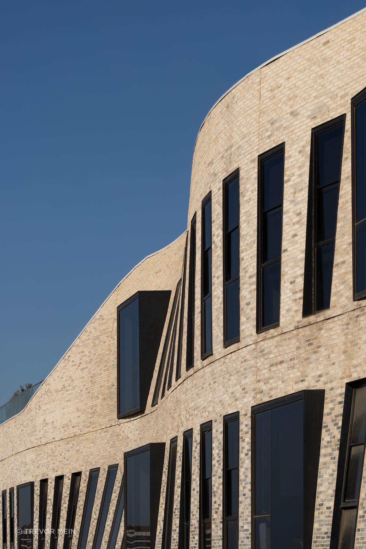 The textured façade of Petersen bricks forms a curved veil.