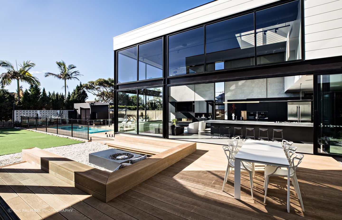 "The extensive decking area features an outdoor dining suite and sunken fire pit with a seating area before flowing into the tennis court, then continuing to wrap around the swimming pool. The Golden Oak decking boards are used as pool coping all the way to the edge."