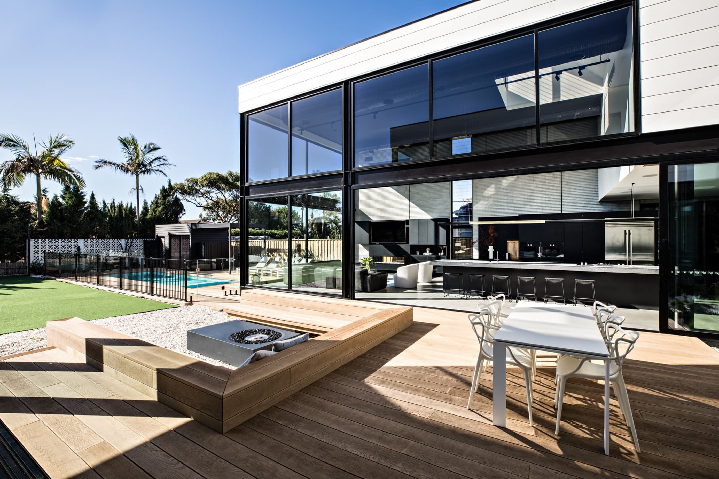 "The extensive decking area features an outdoor dining suite and sunken fire pit with a seating area before flowing into the tennis court, then continuing to wrap around the swimming pool. The Golden Oak decking boards are used as pool coping all the way to the edge."