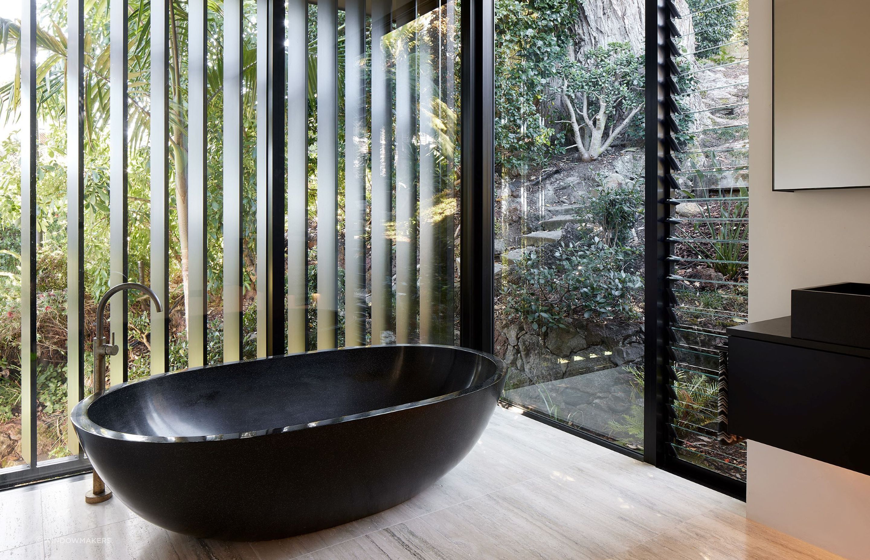 Glass panelling around the statement freestanding tub fully immerses one into the natural surroundings of this Herne Bay home.