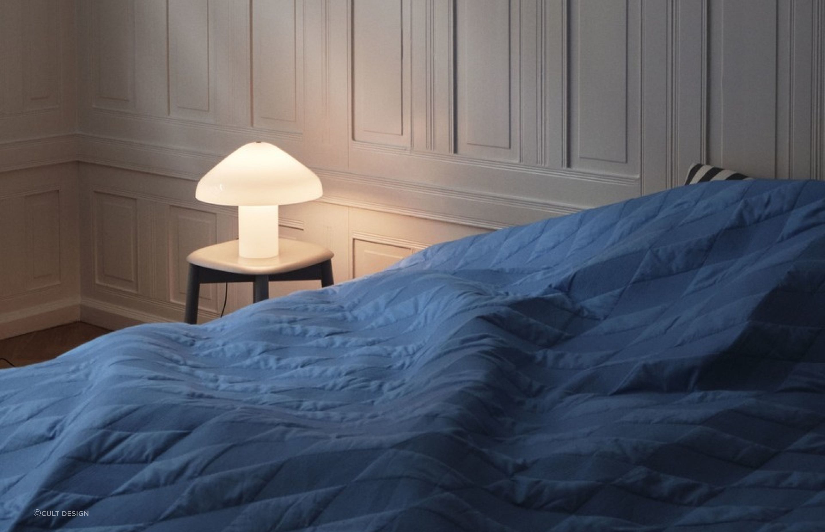 A bedside table can set the stage for a designer lamp like the Pao Glass Table Lamp by HAY.