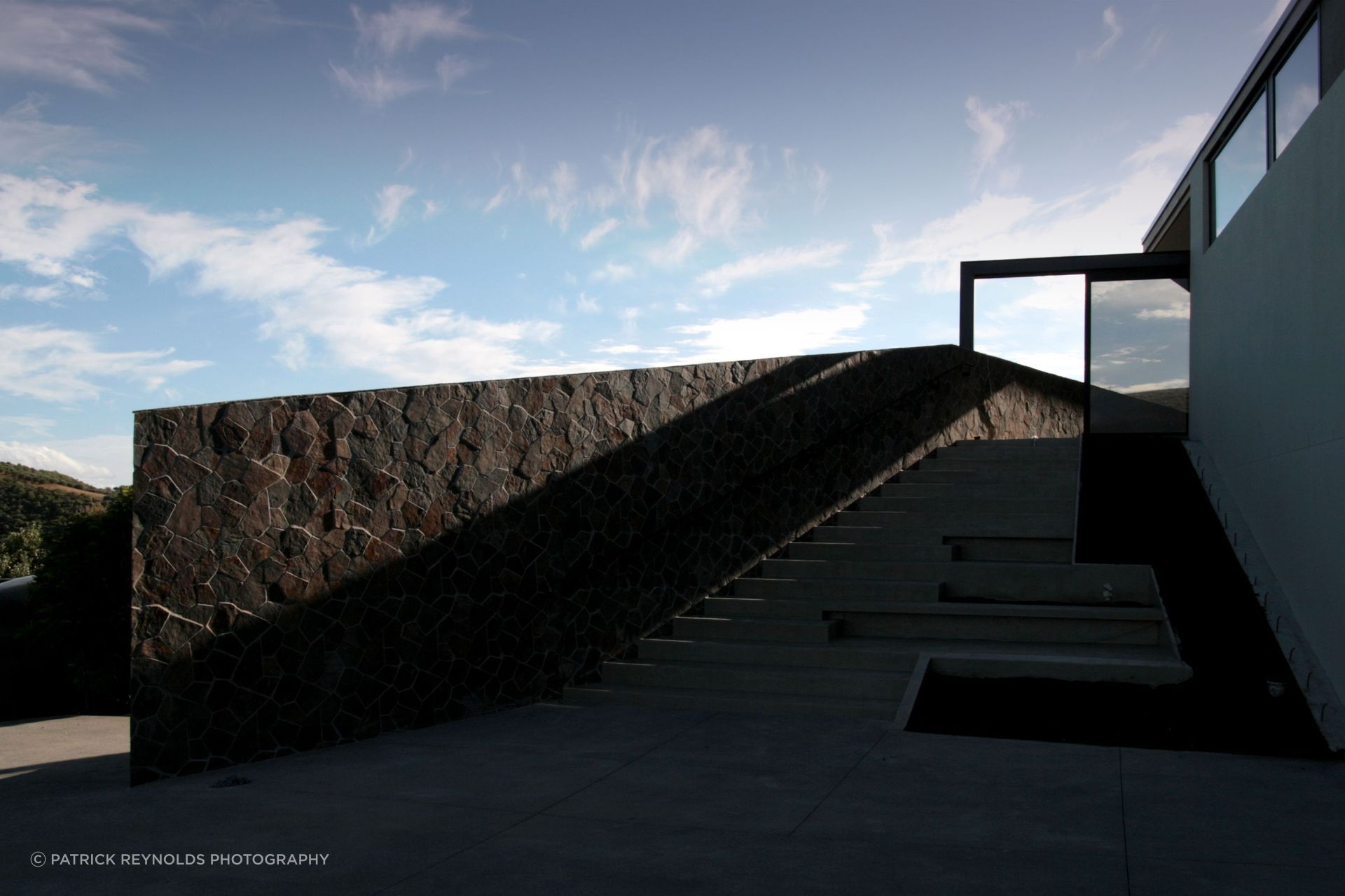 A Waiheke Stone wall defines the entry sequence, its irregular texture catching light and shadow along the stairs | Photography by Patrick Reynolds