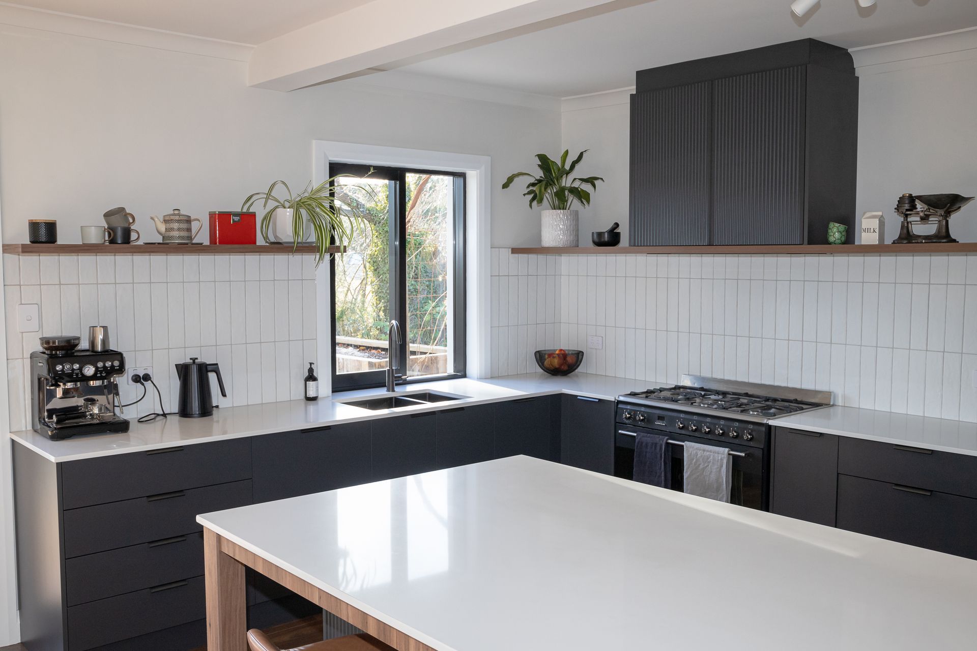 The new kitchen in the Adams Rd project is sleek and modern with black cabinetry, fluted detailing, and timber accents.