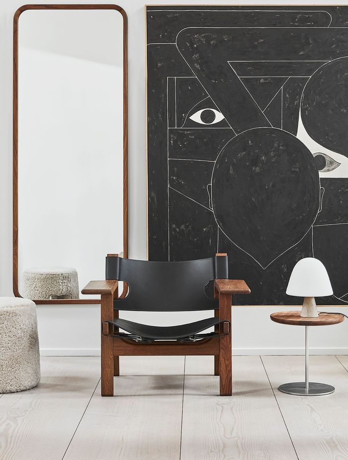 The sleek Silhouette Mirror Rectangle by Fredericia positioned behind an armchair and stool.