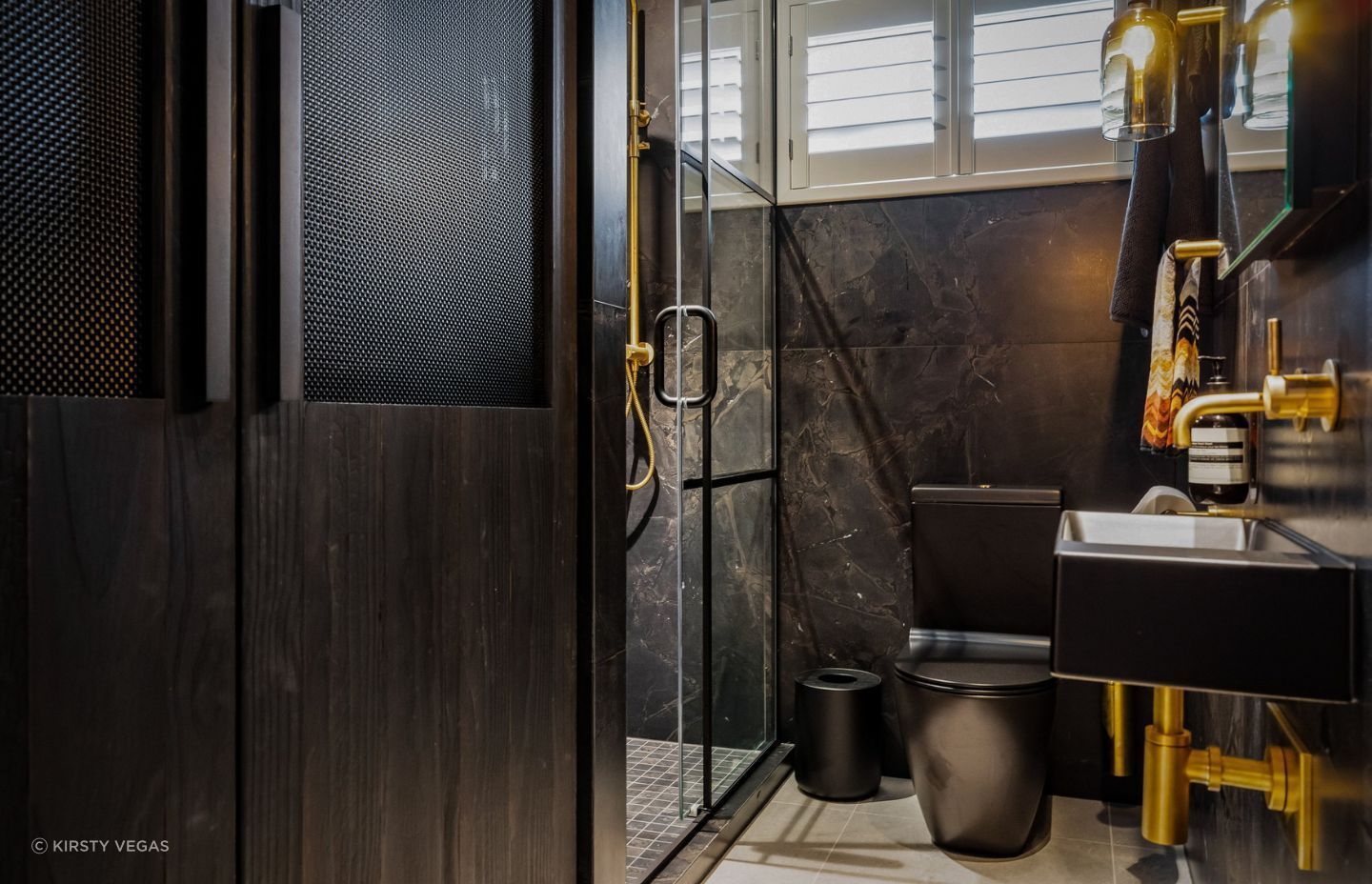A former laundry has been transformed into a stylish guest bathroom, seamlessly concealing a compact laundry behind Shou Sugi Ban and mesh doors.