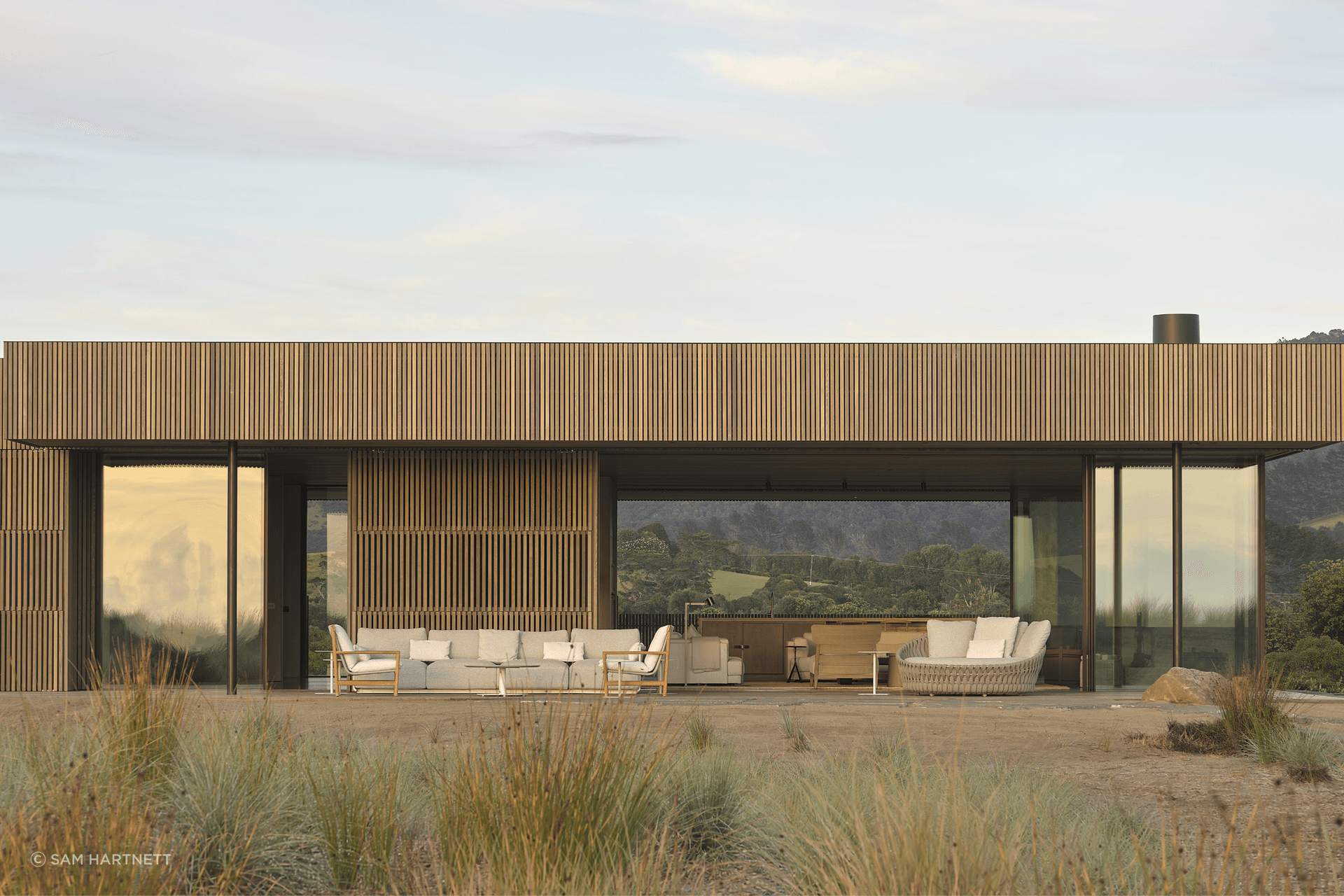 Timber-clad sliding screens protect the home from coastal exposure while allowing the building to become a subdued volume within the dune.