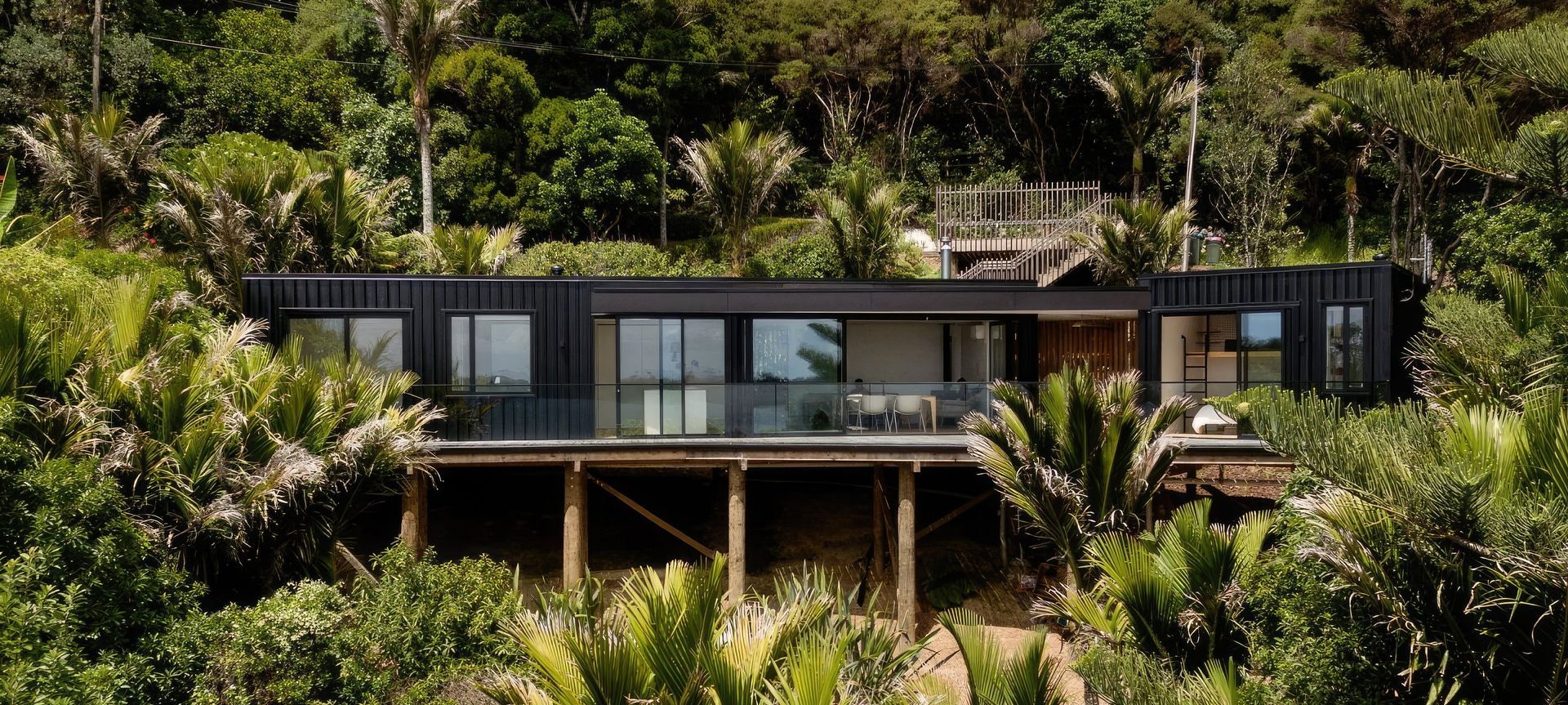 In the picturesque, yet challenging terrain of Waiheke Island, a French couple partnered with Artis Homes to create an affordable yet beautiful home that fits perfectly in its environment. Given the sloping site’s constraints, conventional construction plans like driveways and garages were discarded. Instead, a pragmatic approach was adopted, including a parking platform and walk-down entry stair to preserve the natural surroundings.