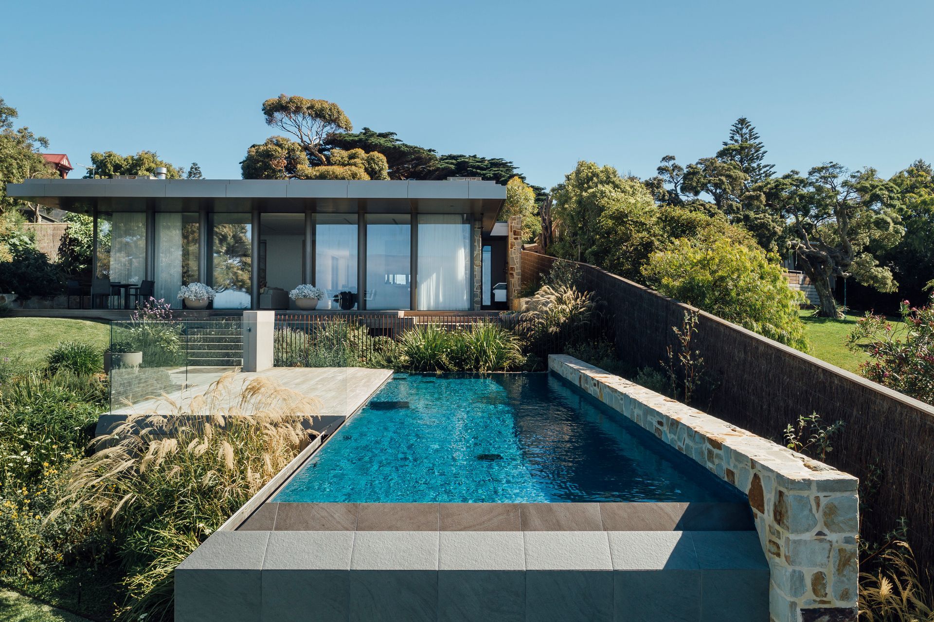 Ornamental grass on the pools left hand side provides a nice contrast with the stone boundary wall on the right. adding this pools visual appeal. Featured project: Erskine - Aloha Pools