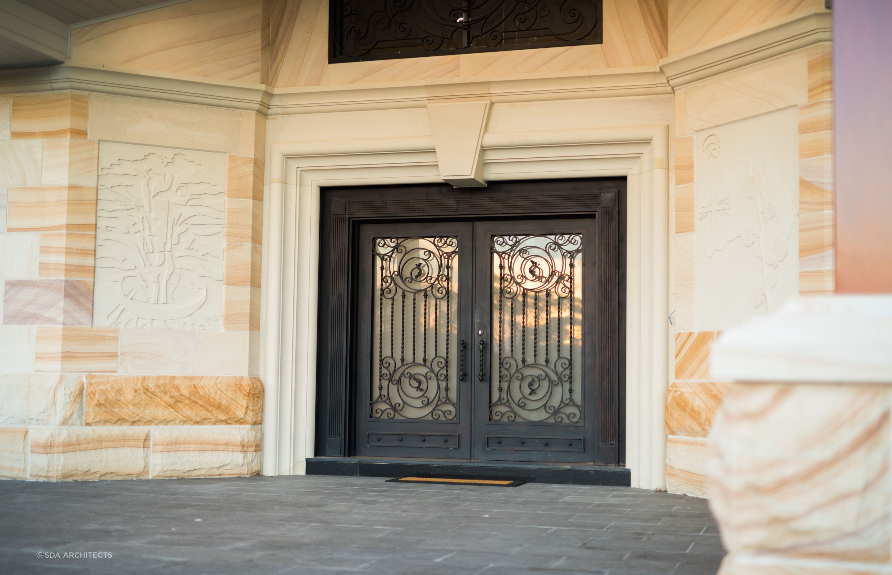 The intricate metal design of these doors contrasts gracefully with the soft, earth-toned surrounding stonework. Featured project: The Rock by SDA Architects